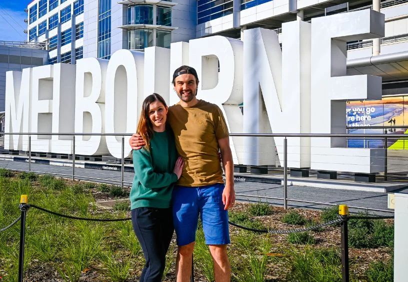 a couple standing in front of the Melbourne airport sign