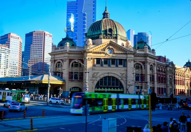 Tram driving through intersection past Flinders street train station in Melbourne