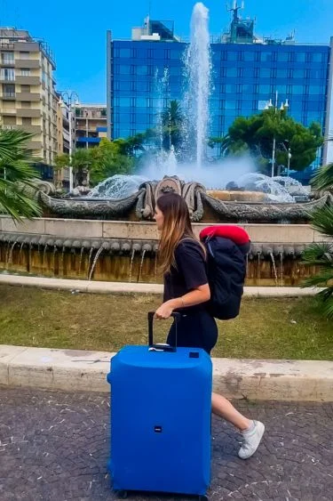 woman walking with a lojel suitcase in front of European fountain
