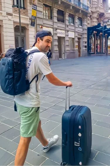 man walking with backpack and suitcase while long-term travelling