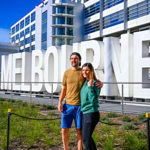 Couple in front of the Melbourne sign at Melbourne Airport