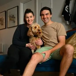 A couple housesitting a small brown spoodle in Melbourne sitting in a couch with Benji