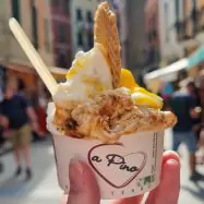 A cup of gelato being presented by a woman with alleyway in background